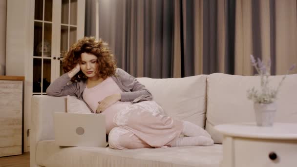 快乐的孕妇在笔记本电脑上看电影 在沙发上摸着肚子 — 图库视频影像