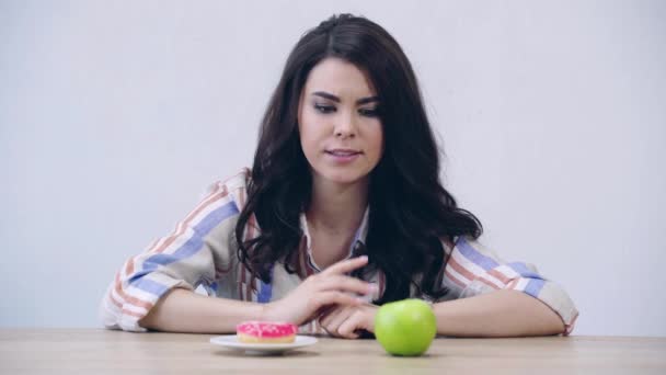 りんごとドーナツを選ぶ混乱した女の子 — ストック動画