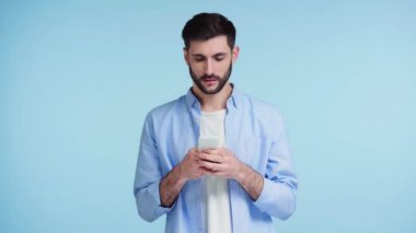 Sakallı adam mavi üzerine izole akıllı telefon kullanıyor. 