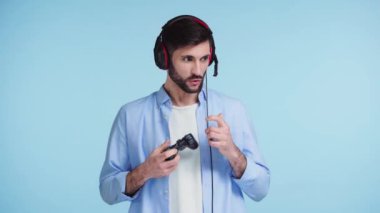 Kyiv, Ukrayna - 21 Kasım 2019: Kulaklıklı duygusal adam mavi üzerinde video oyunu oynuyor