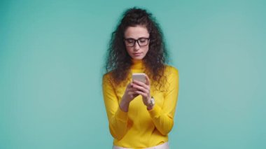 Turkuazda izole akıllı telefon kullanan şok olmuş bir kadın. 