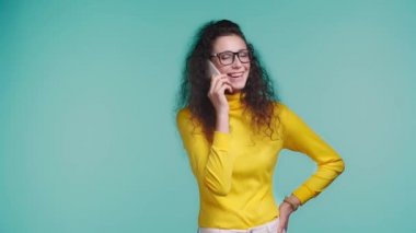 Turkuazda izole edilmiş akıllı telefondan konuşan gülümseyen kadın. 