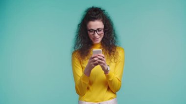 Turkuazda izole edilmiş akıllı telefon kullanan gülümseyen kadın. 