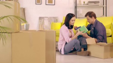 Couple with books sitting on floor near boxes in new home