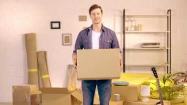 Smiling man putting package and showing thumb up in new home