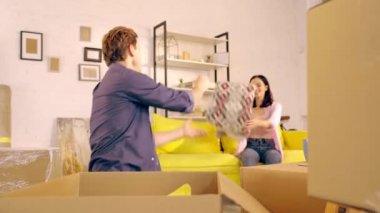 Man unpacking pillow and plaid from box near girlfriend on couch