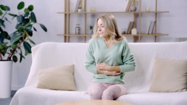 Kanepede oturan ve karın ağrısı çeken bir kadın.