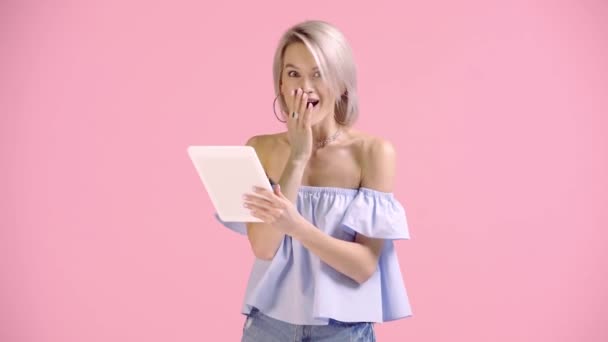 ブロンドの女の子がデジタルタブレットを見せピンクに孤立した親指を見せ — ストック動画