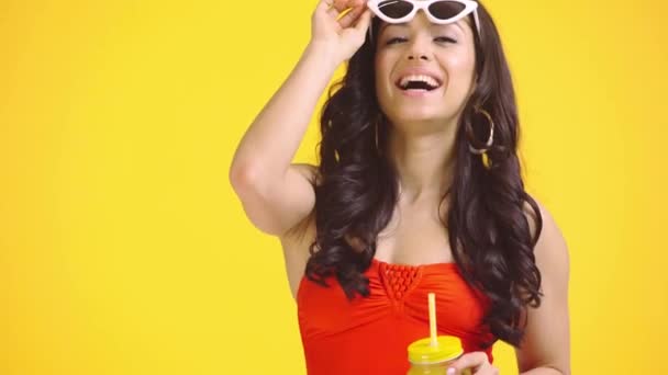 Menina Feliz Com Suco Laranja Tocando Óculos Sol Isolados Amarelo — Vídeo de Stock