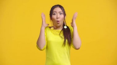 Şaşırmış Asyalı kız sarı üzerine izole edilmiş el kol hareketi yapıyor. 