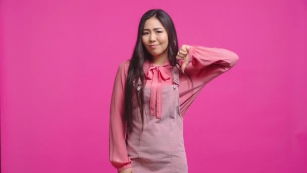 不満なカザフスタン人の少女がピンクで孤立した親指を見せ — ストック動画