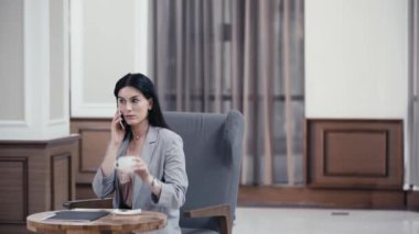 İş kadını akıllı telefondan konuşuyor ve restoran lobisinde kahve içiyor.