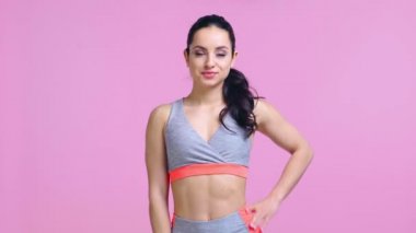 Gülümseyen sporcu kadın pembe üzerine izole bir şekilde baş parmağını gösteriyor. 