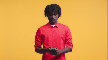 Sinirli Afrikalı Amerikalı adam akıllı telefondan konuşuyor ve sarı ışıkta izole edilmiş el kol hareketleri yapıyor.