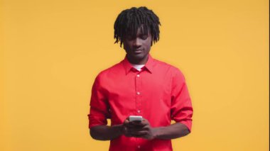 Afro-Amerikalı bir adam akıllı telefondan konuşuyor ve sarıda yalnız bir şekilde gülümsüyor.