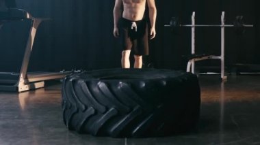 Kaslı adam araba lastiğiyle egzersiz yapıyor. 