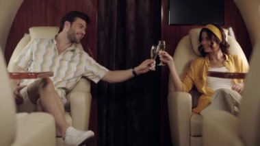 Mutlu çift uçakla seyahat ederken şampanya bardaklarını tokuşturuyor.