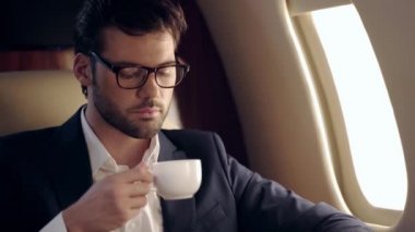 Yakışıklı işadamı uçakla seyahat ederken kahve içiyor.