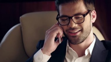 Gülümseyen iş adamı gazete okuyor ve uçakta akıllı telefondan konuşuyor.