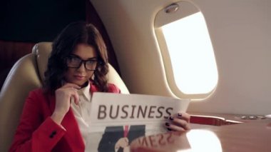 Uçakla seyahat ederken iş gazetesi okuyan dikkatli bir iş kadını.