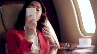İş kadını akıllı telefondan konuşuyor ve uçakla seyahat ederken zamanı kontrol ediyor.