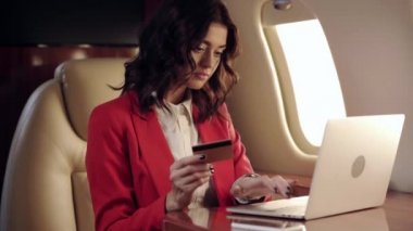 İş kadını laptop kullanıyor ve uçakla seyahat ederken kredi kartı gösteriyor.