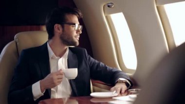 İş adamı elinde kahve tutuyor ve uçakla seyahat ederken aydınlatmaya bakıyor.