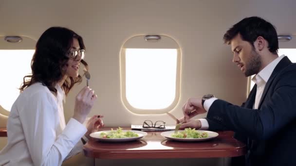Νέοι Επιχειρηματίες Που Μιλούν Και Τρώνε Σαλάτα Ενώ Ταξιδεύουν Αεροπλάνο — Αρχείο Βίντεο