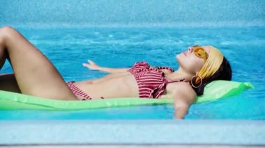 Güneş gözlüklü kadın yazın havuzda yüzer.