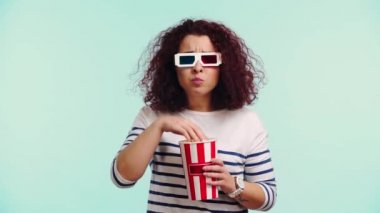 Üç boyutlu gözlüklü korkmuş kız film izliyor ve turkuazda izole edilmiş patlamış mısır yiyor.