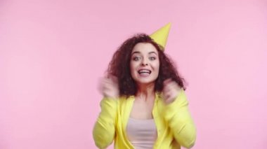 Parti şapkalı mutlu kız el çırpıyor ve pembe üzerinde yalnız dans ediyor.
