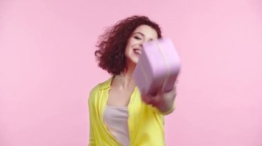 Mutlu kız pembe üzerinde izole edilmiş hediye kutusunu işaret ediyor.
