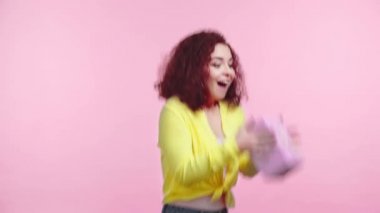 Merak uyandıran kıvırcık kız pembe üzerine izole edilmiş hediye kutusunu sallıyor.