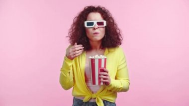 Yoğunlaşmış kız film izliyor ve pembe üzerine izole edilmiş patlamış mısır yiyor.