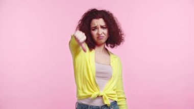Pembe üzerine izole edilmiş kameraya bakarken baş parmağını gösteren hoşnutsuz bir kız.