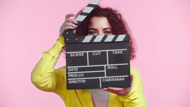 Chica Rizada Oscureciendo Cara Con Clapboard Aislado Rosa — Vídeos de Stock