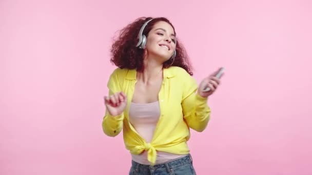 快乐的女孩在用粉色隔离的无线耳机中跳舞和唱歌 — 图库视频影像