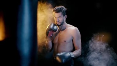 Boksör siyah arka planda boks eldivenleriyle kum torbasına vuruyor.