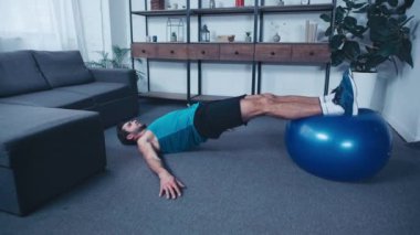 Genç sporcu evde spor topuyla egzersiz yapıyor.
