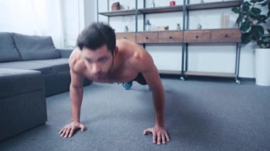 Kaslı, üstsüz sporcu evde yerde şınav çekiyor.