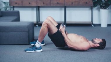 Üstsüz, kaslı sporcu antrenmanı. Ağırlığı evde yerde.