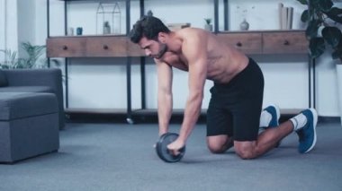 Genç üstsüz sporcu antrenmanı. Evde spor tekerleği var.