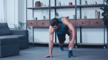 Genç sporcu evde tek bacaklı tahta duruşuyla egzersiz yapıyor.
