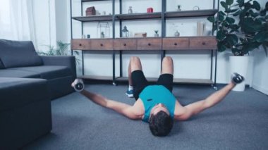 Genç sporcu evde yerde yatarken dambıllarla antrenman yapıyor.