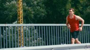 Genç sporcu köprüde koşuyor ve dinlenmek için duruyor.
