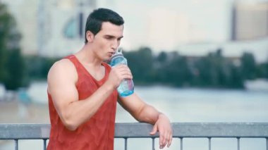 Genç sporcu köprüde duruyor ve spor şişesinden içiyor.