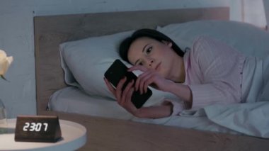 Gece yatakta akıllı telefon kullanan bir kadın.