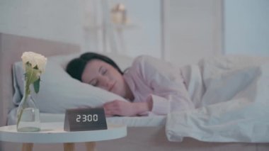 Saat ve çiçeğin seçmeli odağı gece uyuyan bir kadının yanındaki masada. 