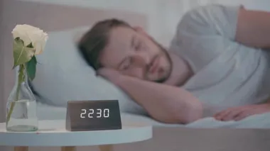 Saatin seçici odağı ve geceleri yatakta uyuyan adamın yanındaki masada yükseldi.