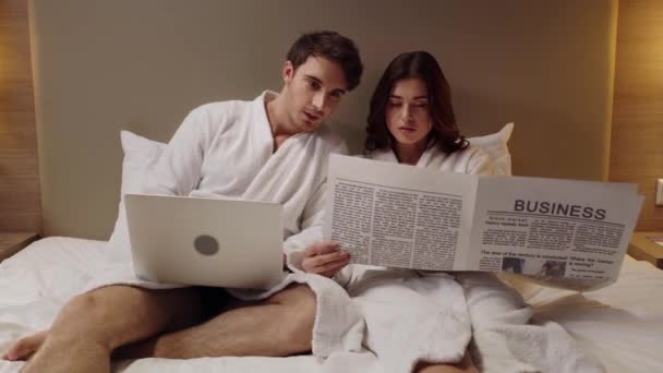 Hombre Con Portátil Mujer Con Periódico Descansando Cama Habitación Hotel — Vídeo de stock